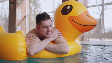 happy-male-visitor-of-swimming-pool-or-thermal-bath-is-floating-on-inflatable-duck-portrait